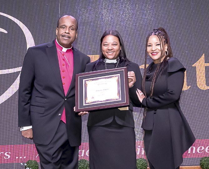 Nefertiti Morris smiling and holding her framed ordination certificate between two people at her Elder ordination ceremony